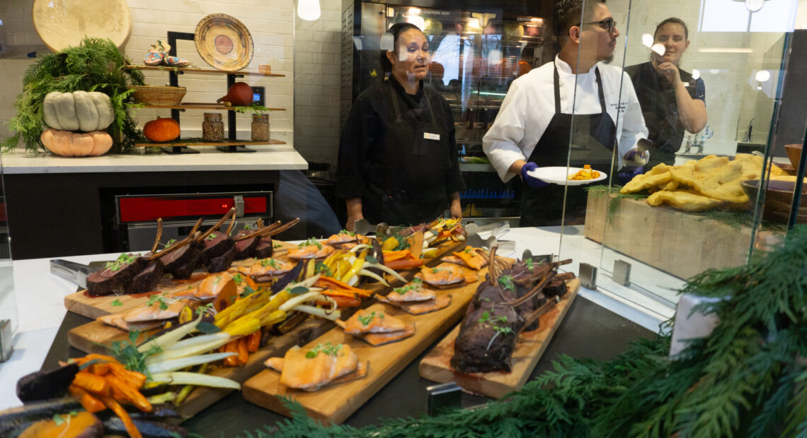 Trays of elk, trout, and root vegetables behind a glass panel.