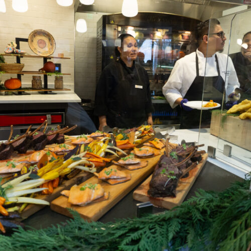 Trays of elk, trout, and root vegetables behind a glass panel.