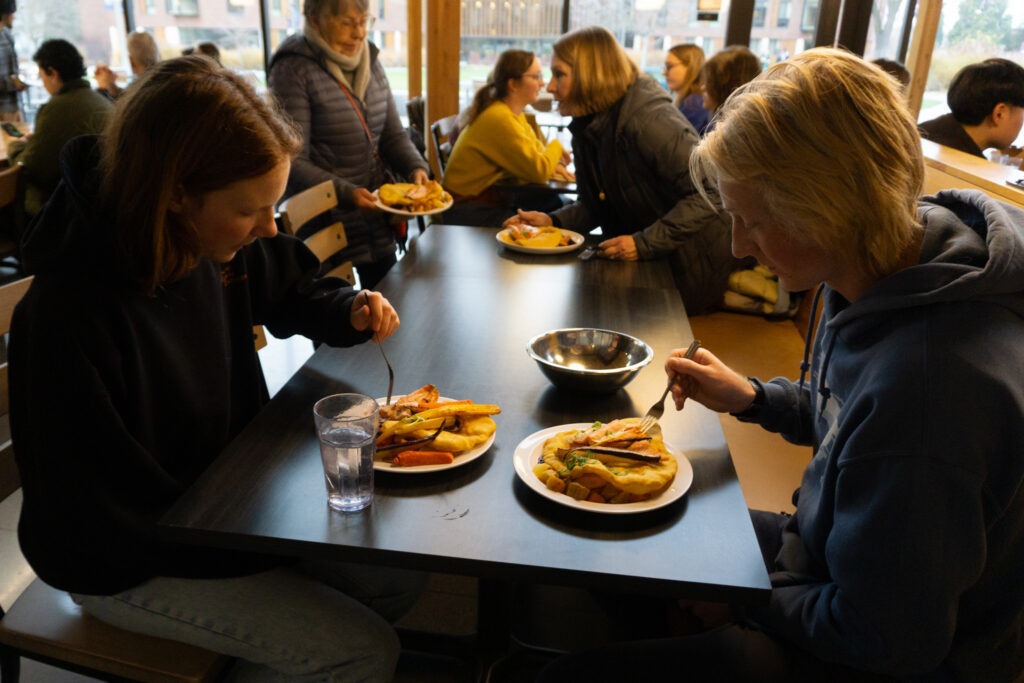 Two students eat from plates with trout and root vegetables.