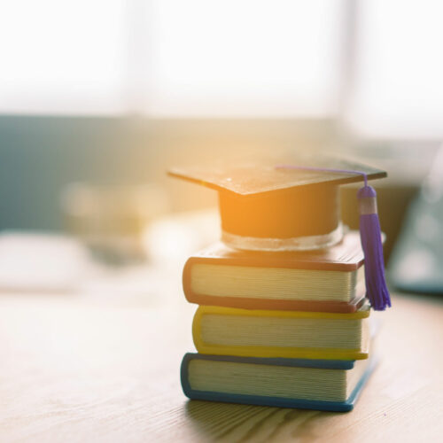 Libros y un birrete reposan sobre un escritorio. (Crédito: Adobe Stock Photos)