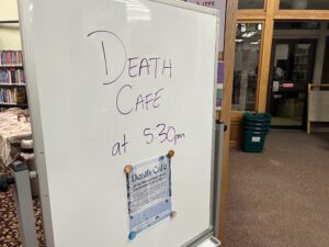 A whiteboard with the words "Death Cafe at 5:30 PM" is on display at a library.