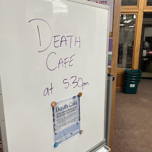 A whiteboard with the words "Death Cafe at 5:30 PM" is on display at a library.