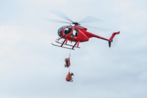 a red helicopter slings bighorn sheep in the air