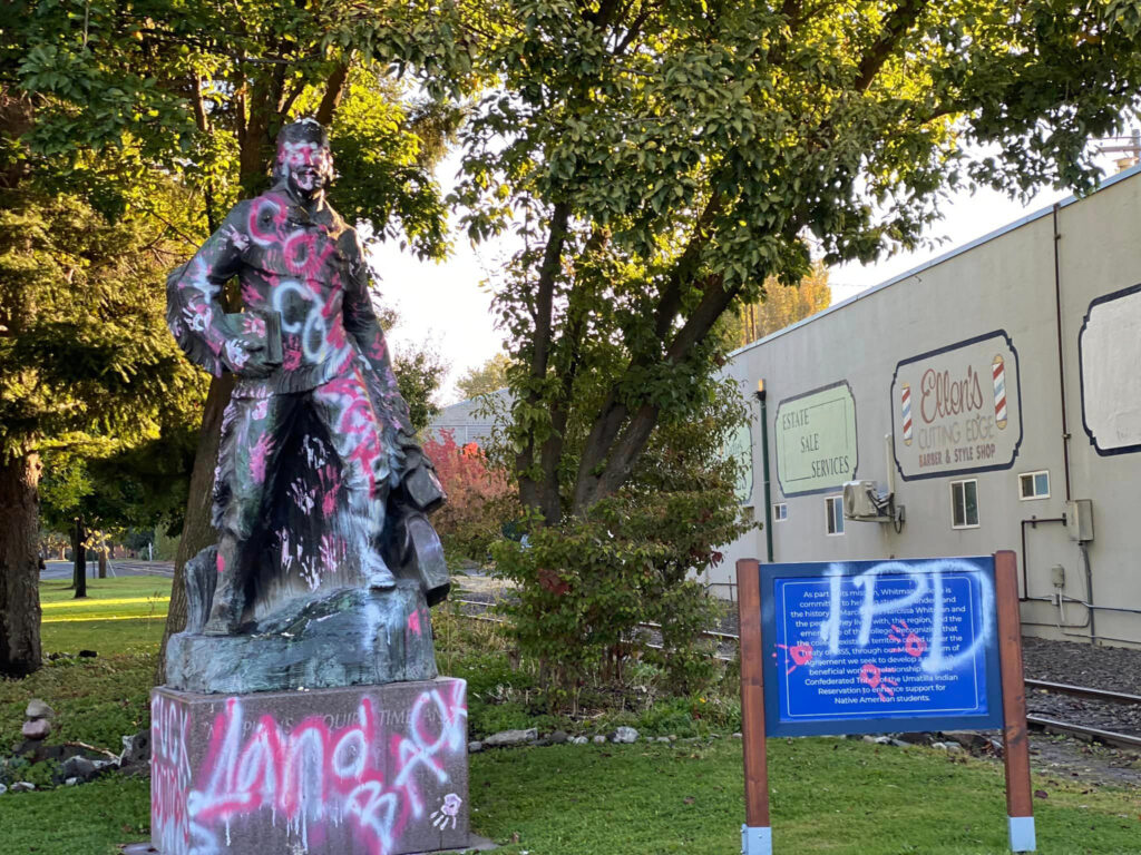 A statue is vandalized with the words "colonizer" and "land back."