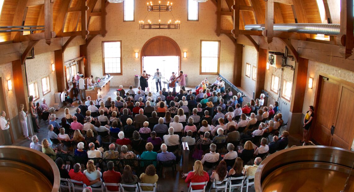 An audience listens to a quintet in a large room with arched wooden ceilings.