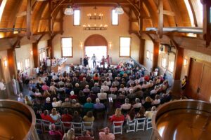 An audience listens to a quintet in a large room with arched wooden ceilings.