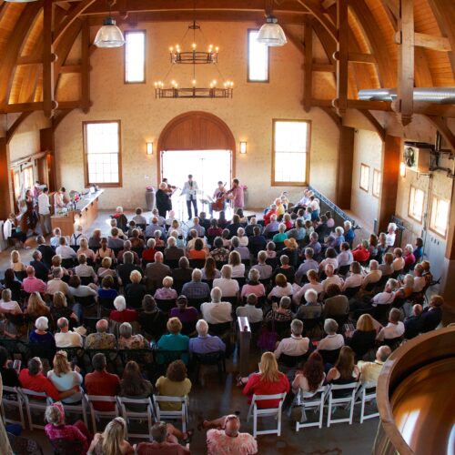 An audience listens to a quintet in a large room with arched wooden ceilings.