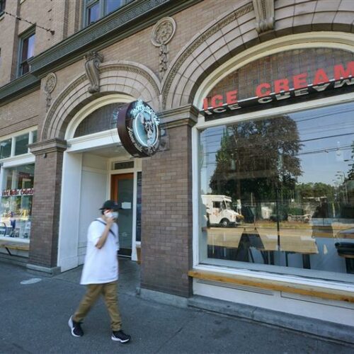 A person walks by a tan, brick building. The sign outside the building reads "Molly Moon's Homemade Ice Cream."