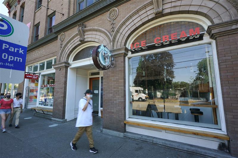 A person walks by a tan, brick building. The sign outside the building reads "Molly Moon's Homemade Ice Cream."