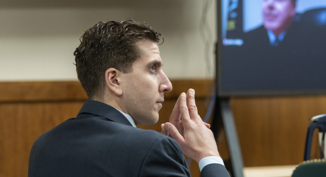 A side profile of Bryan Kohberger in a suit shows him sitting in a courtroom with his fingers pressed together.