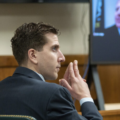 A side profile of Bryan Kohberger in a suit shows him sitting in a courtroom with his fingers pressed together.