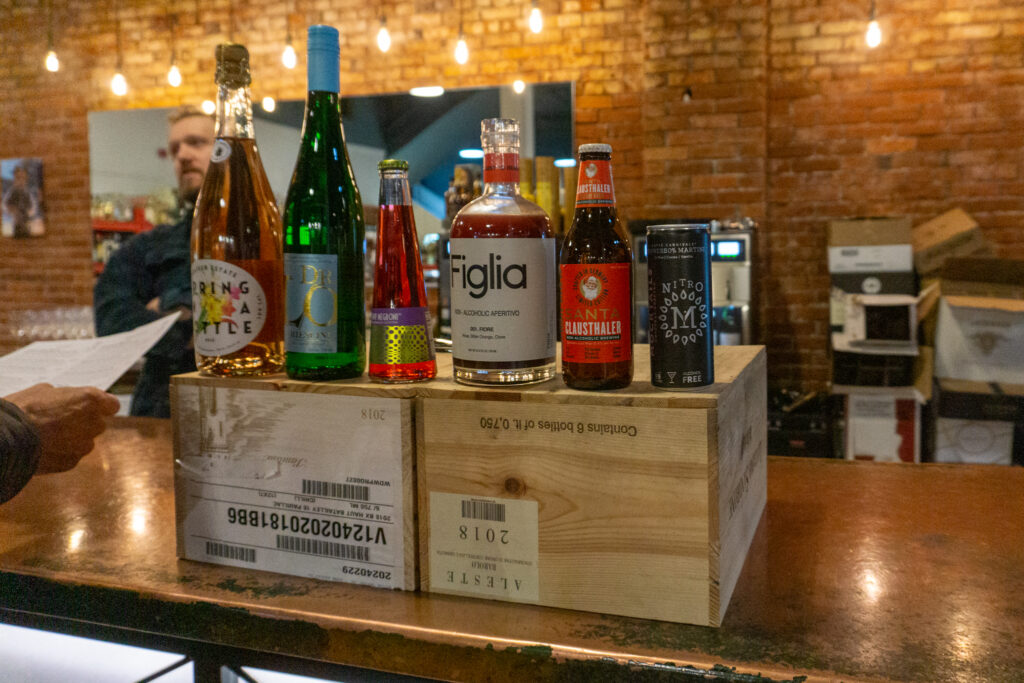 Six bottles sit on top of wooden cases with twinkly lights and a brick wall in the background.