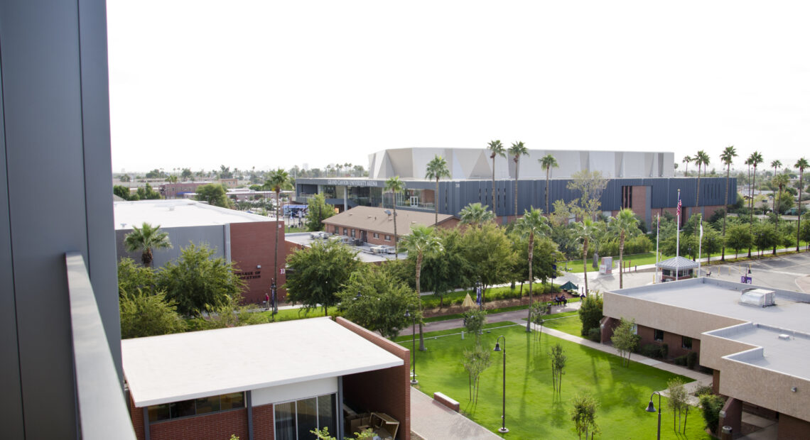 A view of a college campus from a higher vantage point. There is gray sky and palm trees surrounding the buildings on the campus.