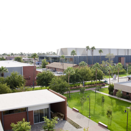 A view of a college campus from a higher vantage point. There is gray sky and palm trees surrounding the buildings on the campus.