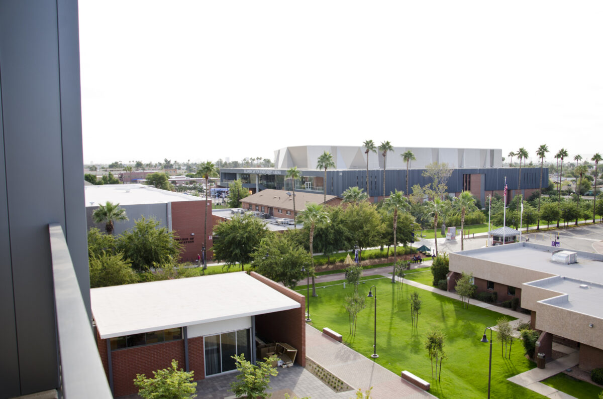 A view of a college campus from a higher vantage point. There is gray sky and palm trees surrounding the buildings on the campus.