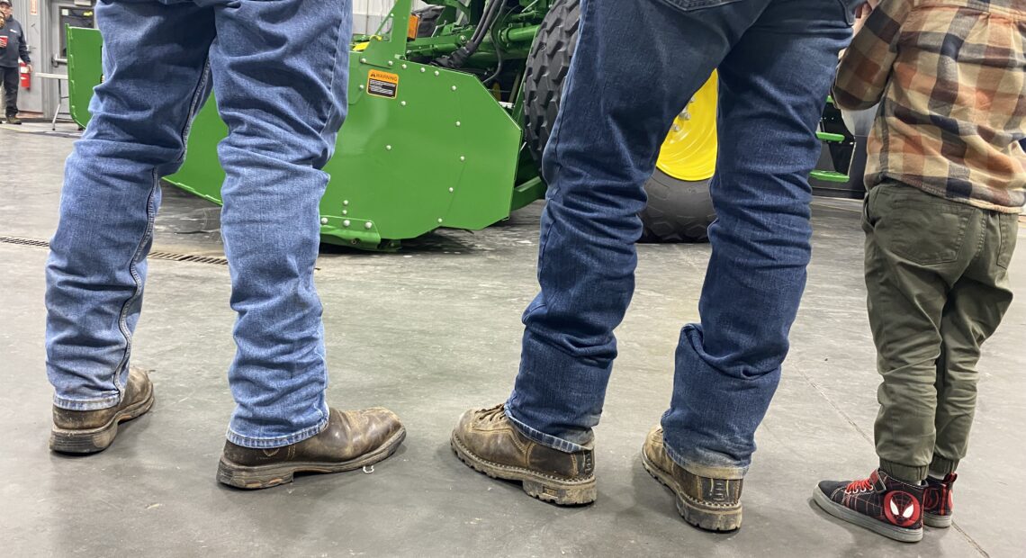 Farmers, and a future farmer, regard a new John Deere swather at RDO, a large tractor dealership in Pasco.