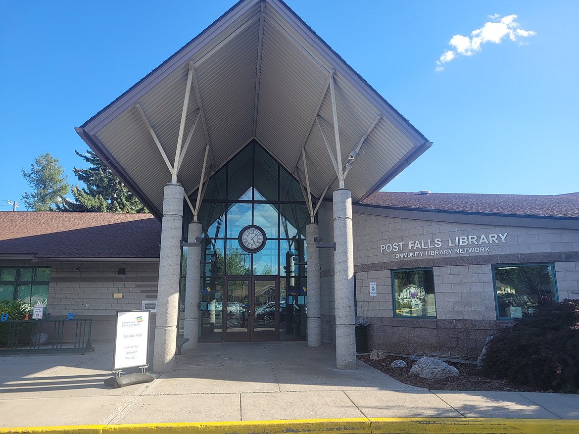 A photo shows the Post Falls Library framed by a bright blue sky with a single cloud. 