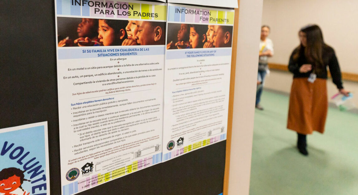 Flyers in English and Spanish are viewed up close. They are posted on a wall. In the background, a person walks by.