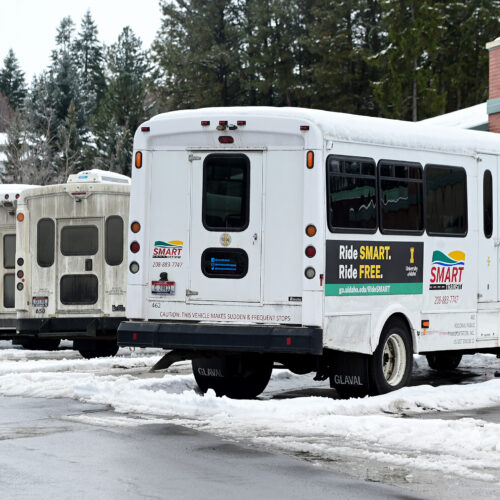 A row of small, white buses are parked outside in a parking lot. There is snow on the ground.