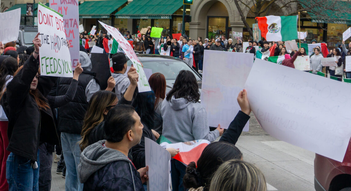 Group of people holding handmade signs and Mexican flags.