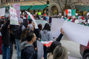 Group of people holding handmade signs and Mexican flags.