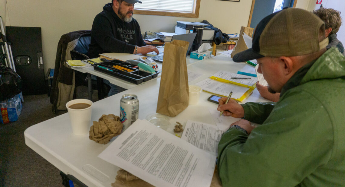 A man in a green jacket and baseball cap fills out a worksheet.