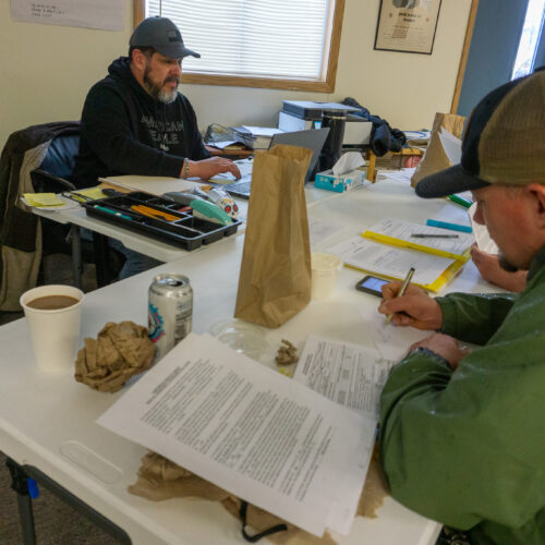 A man in a green jacket and baseball cap fills out a worksheet.