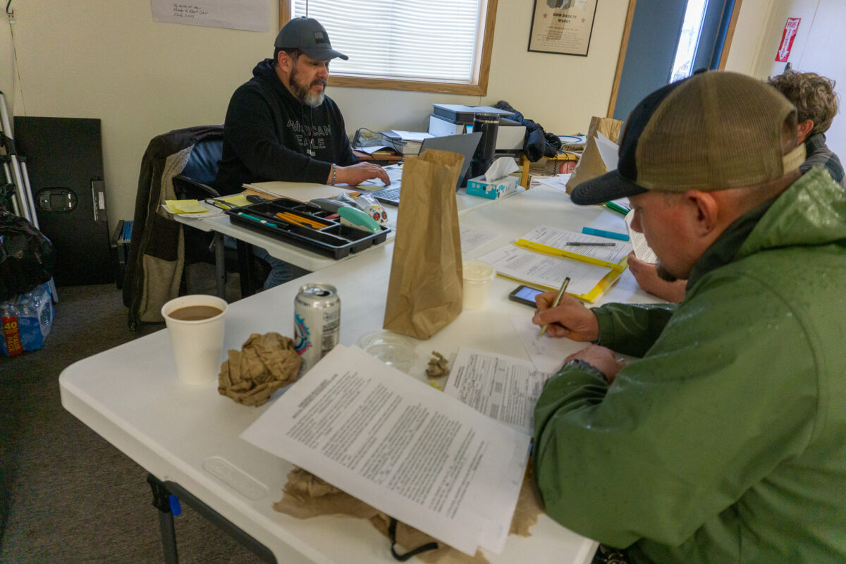 A man in a green jacket and baseball cap fills out a worksheet.