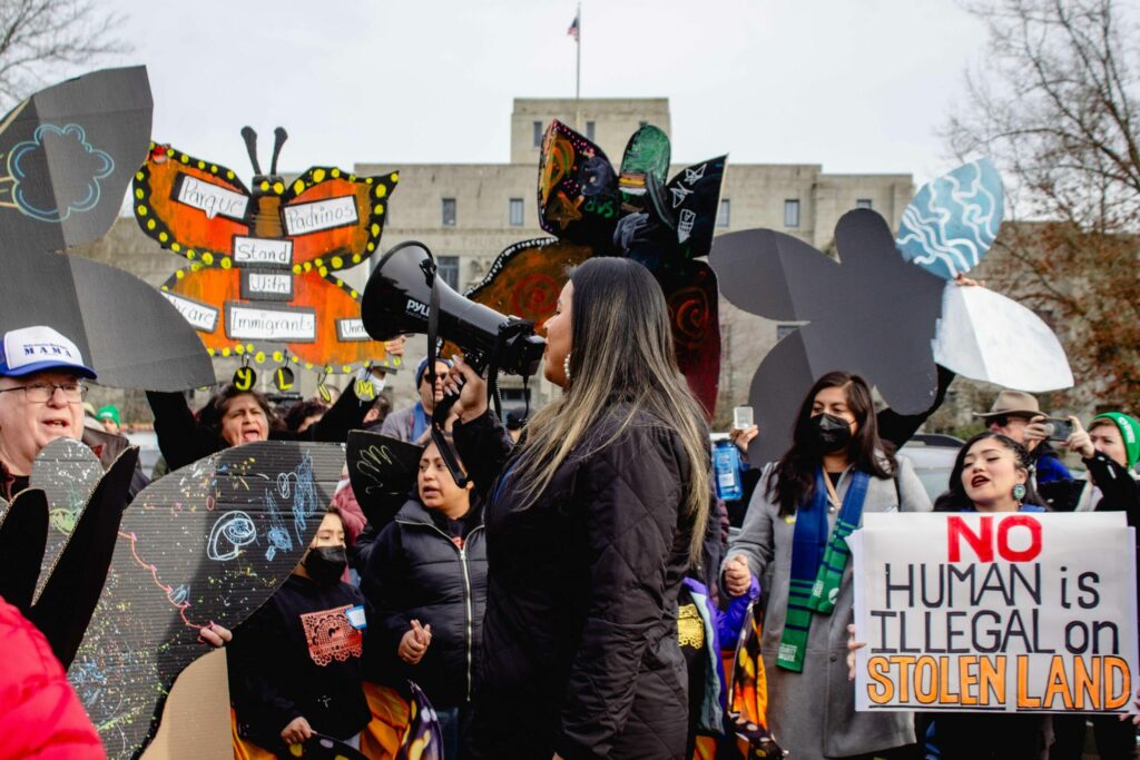 A person speaks into a megaphone. A group of people stand behind them, holding signs.