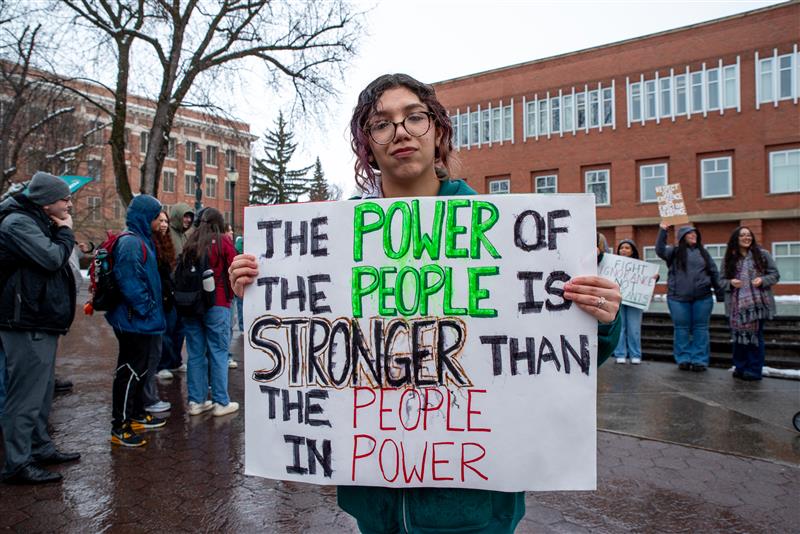 A person holds a sign that reads: "The power of the people is stronger than the people in power." 