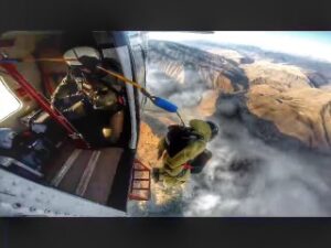 A man in all yellow jumps from a plane over a large wildfire seen in the distance.