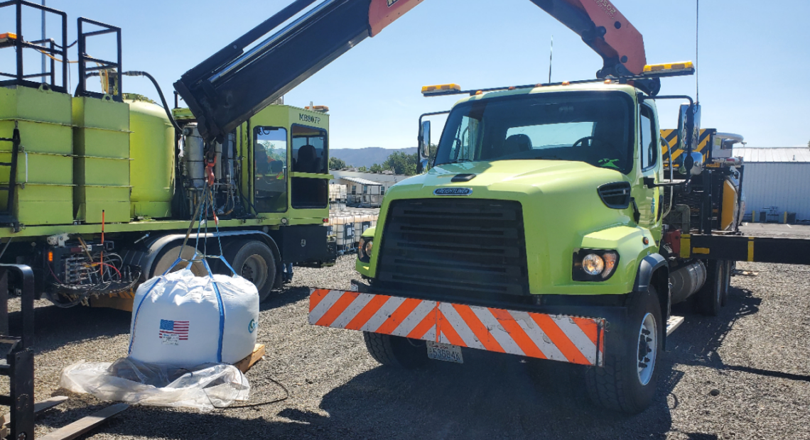 A large bright green truck sits on a gravel road.