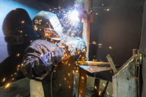 A welder in a helmet connects two pieces of metal as sparks fly.