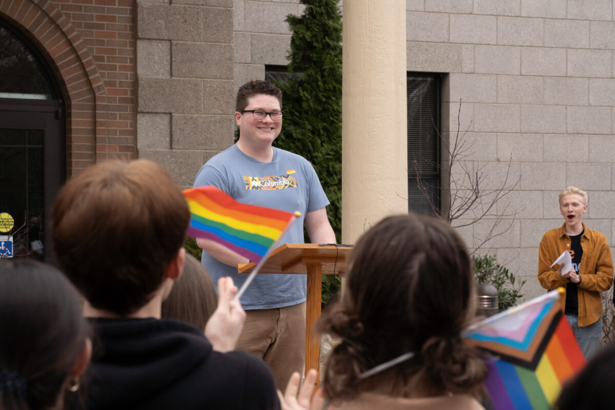 A man in a blue shirt smiles at people holding rainbow flags.