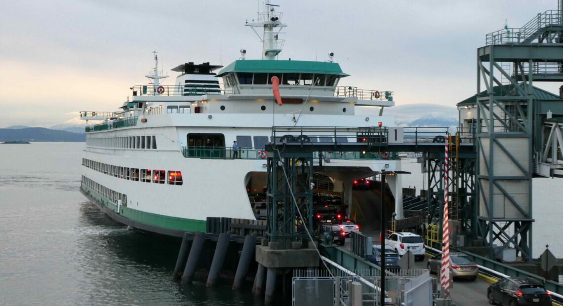 A Washington state ferry approaches a dock. The sky behind the vessel is gray and cloudy.